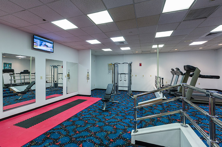 Interior shot of the recreational fitness center at our family friendly resort in Kissimmee, FL. Three mirrors mounted on the wall and exercise equipment placed around room