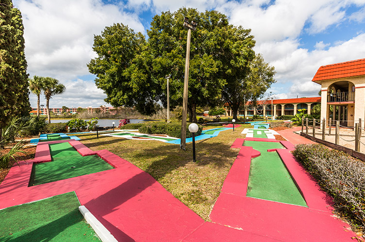 exterior shot of the miniature golf course at our family friendly resort in Kissimmee, FL surrounded by trees & large pond in the background