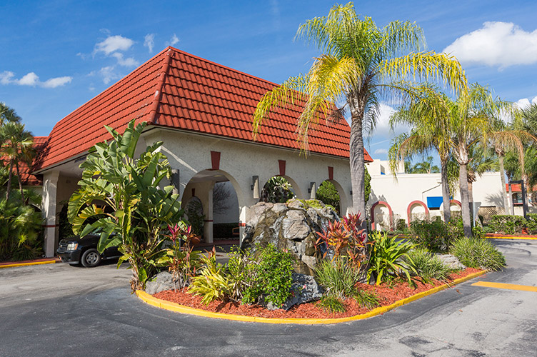 Exterior shot of the front entrance to our family friendly hotel in Kissimmee, FL with red roofing, green palm trees, and clear skies in the background