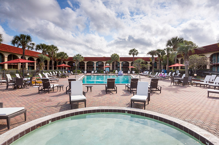 exterior shot of the pool & hot tub at our family friendly resort in Kissimmee, FL. Brick pavers patio, and folding beach chairs nearby
